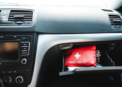 Intérieur de voiture avec boîte à gants ouverte dévoilant une trousse de premiers secours rouge à l’intérieur et un jeu de clés accroché sur le côté. Intérieur de voiture avec boîte à gants ouverte dévoilant une trousse de premiers secours rouge à l’intérieur et un jeu de clés accroché sur le côté.
